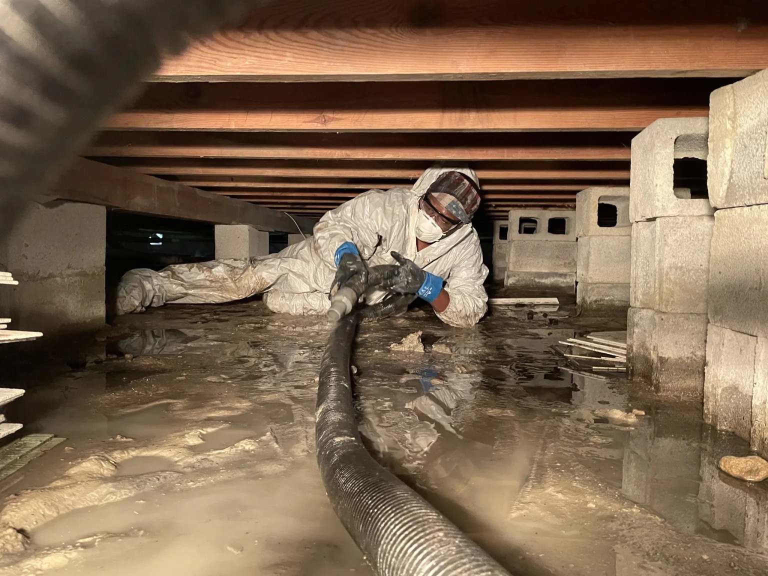 Crawl space cleaning in Olympia, WA — technician removing mud and standing water debris beneath the home